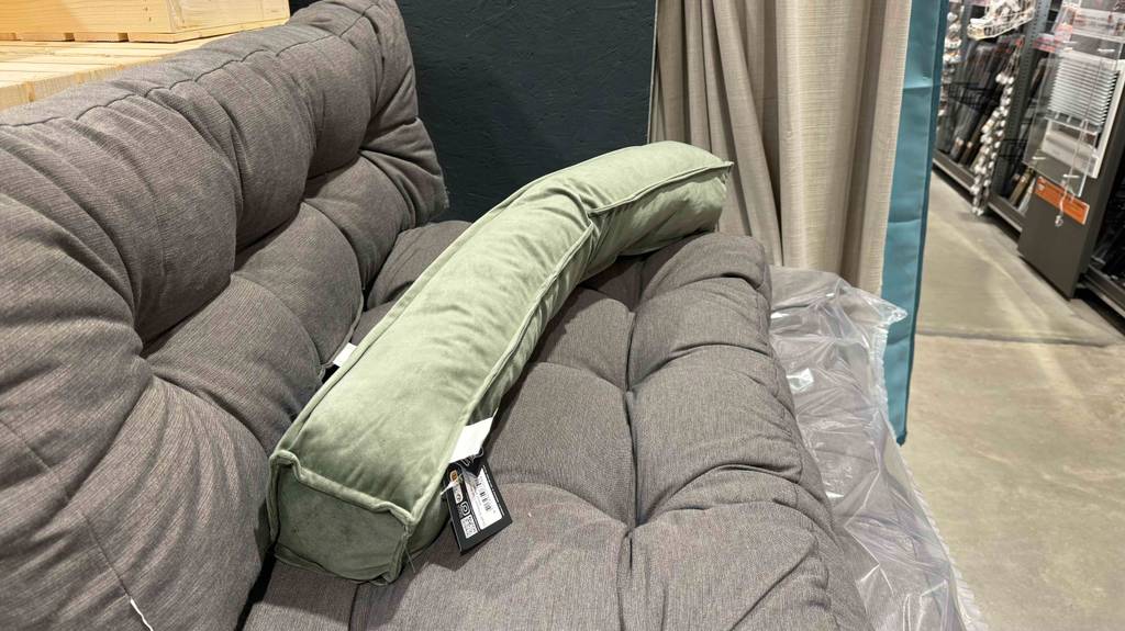 Zugluftstopper-Test: Ein grünes Modell liegt auf einem grauen Sofa im Verkaufsbereich.