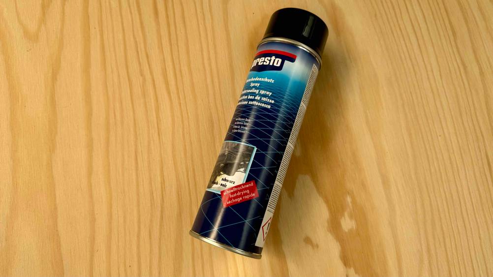Eine Dose des getesteten Unterbodenschutzes von schräg unten seitlich auf einer Holzfläche liegend.