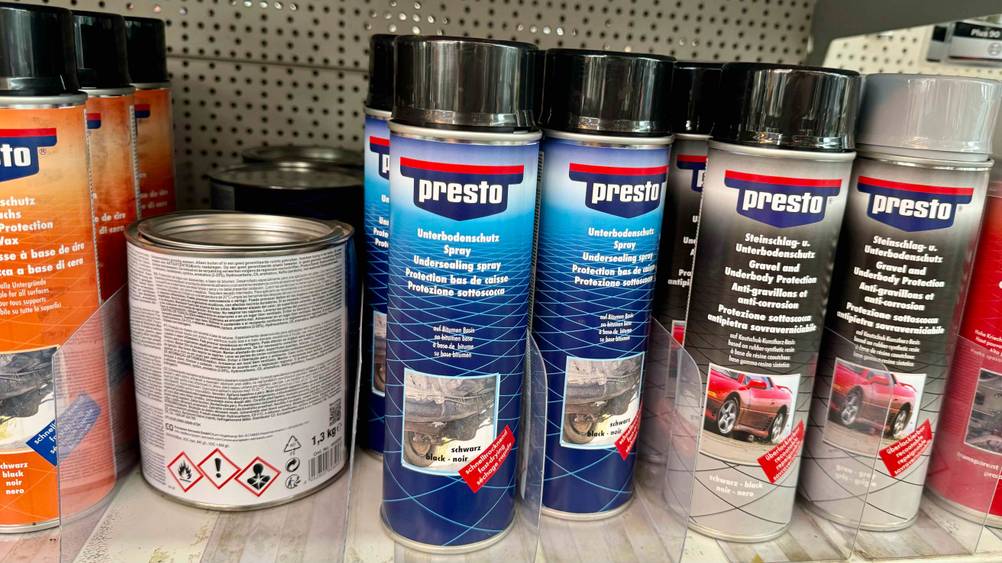 Mehrere Dosen des Unterbodenschutzes im Test in einem Regal neben anderen Produkten.