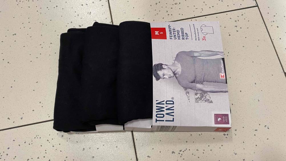 Mehrere Unterhemden für Herren im Test: Auf dem Boden liegt einer 3er-Stück-Packung mit Unterhemden für Herren. 
