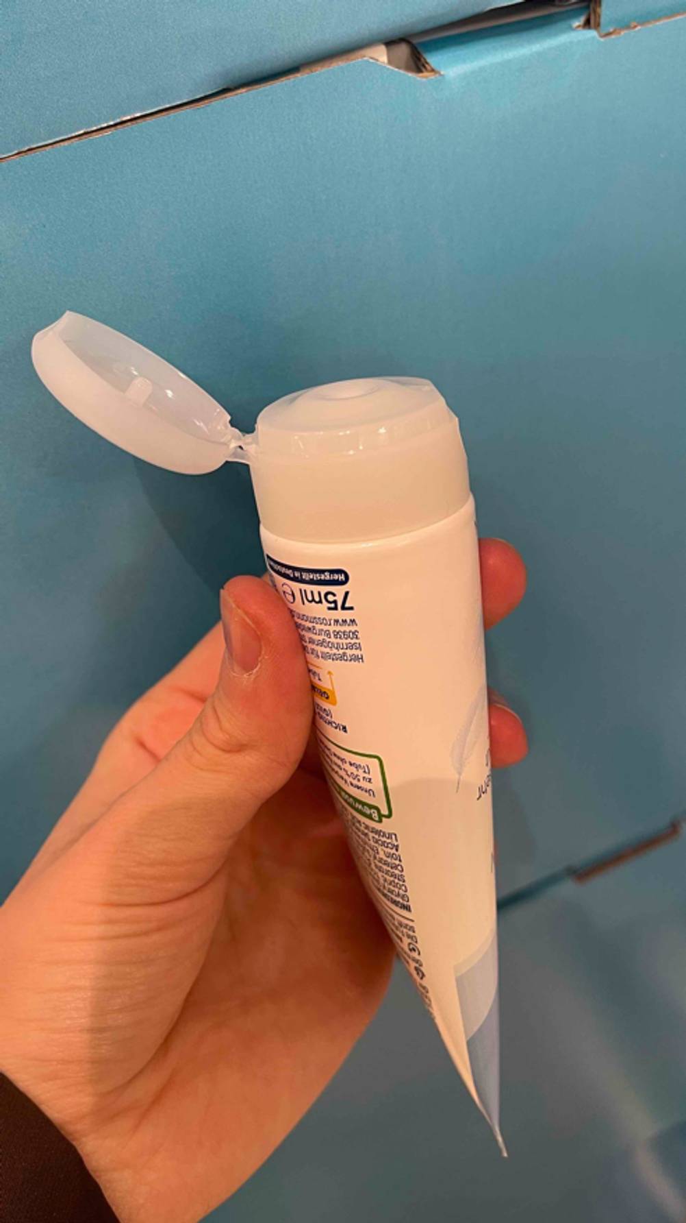 Eine Hand hält eine Tube getestete Urea-Fußcreme mit offenem Deckel.