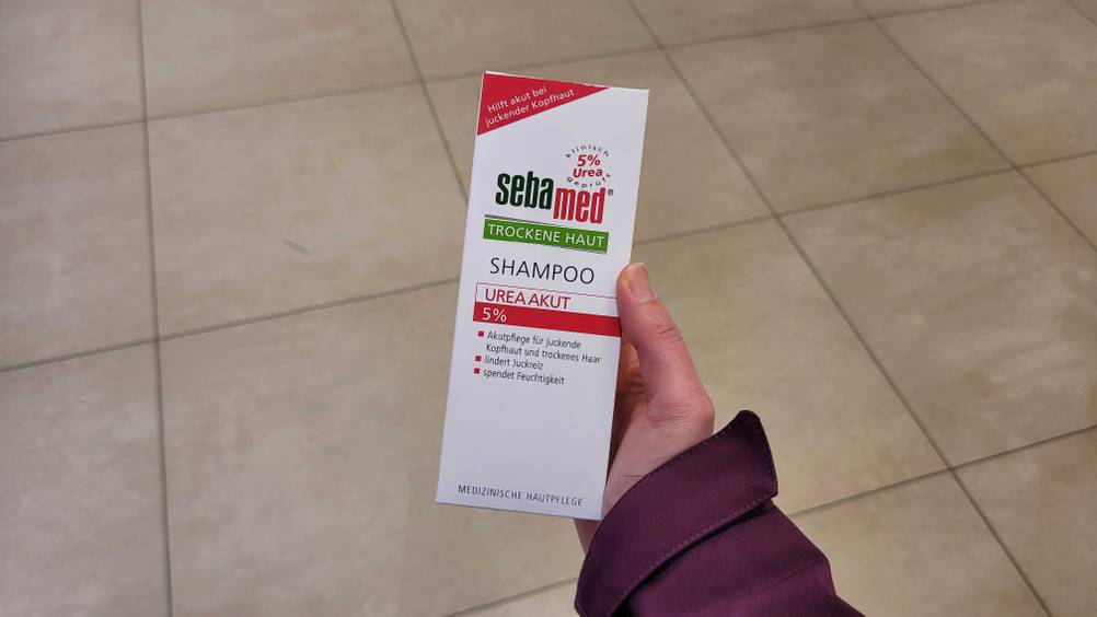 Eine Hand hält eine Packung des getesteten Urea-Shampoos hoch.
