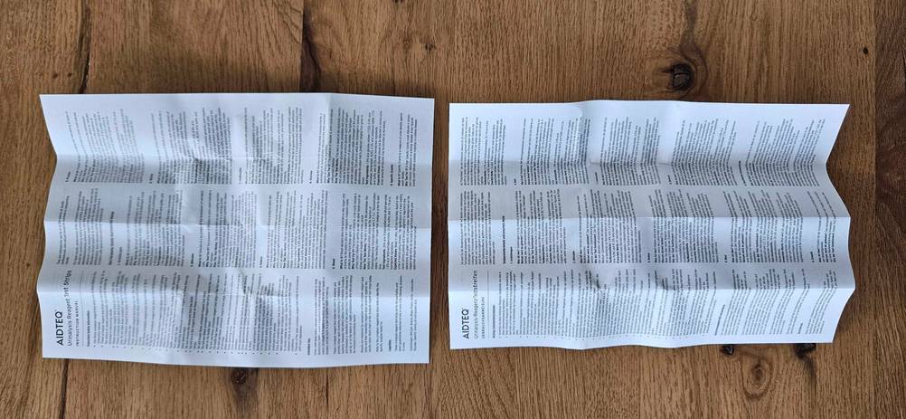 Auf einer Holzoberfläche befinden sich Produktinformationen und Warnhinweise von getesteten Urinteststreifen.