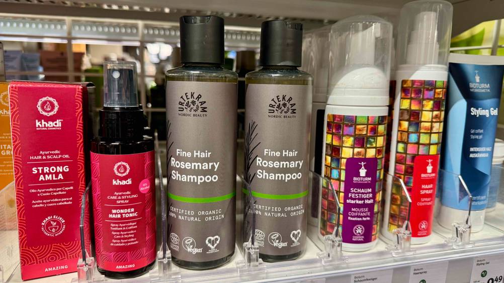 Mehrere Flaschen des Urtekram-Shampoo im Test in einem Verkaufsregal neben anderen Produkten.