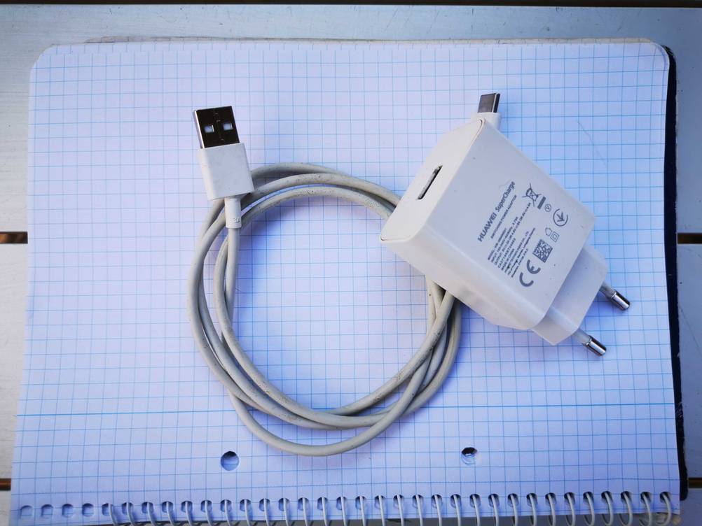 Auf einem Notizblock liegt ein getestetes USB-Schnellladegerät mit seinem Kabel.