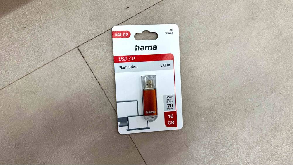 Auf einem hellen Boden liegt ein getesteter USB-Stick (16GB) in seiner Originalverapckung.