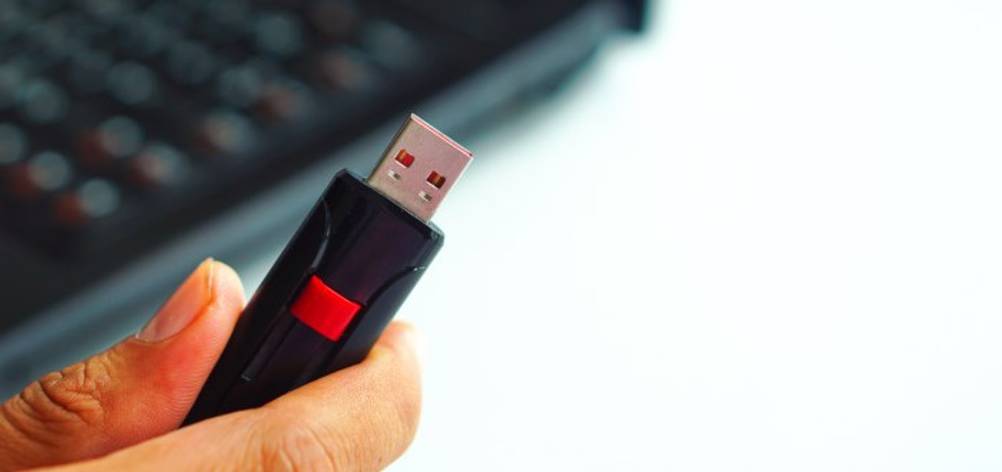 Nahaufnahme einer Frauenhand, die einen getesteten 256-GB-USB-Stick mit ausfahrbarem USB-Stecker in der Hand hält. Im Hintergrund sieht man ein verschwommenes Notebook.
