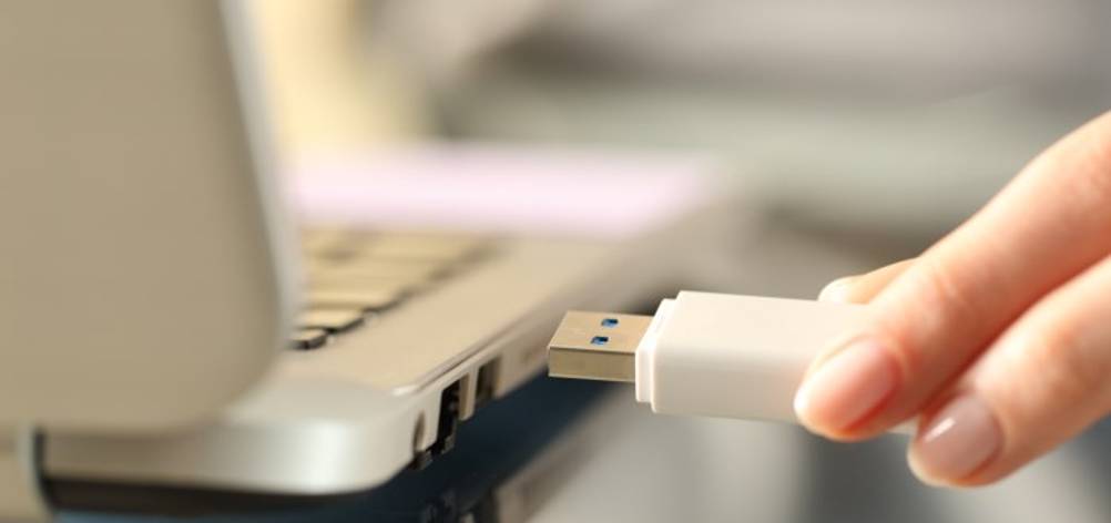Nahaufnahme einer Frauenhand, die einen getesteten weißen USB-Stick (256 GB) in ein weißes Notebook steckt.