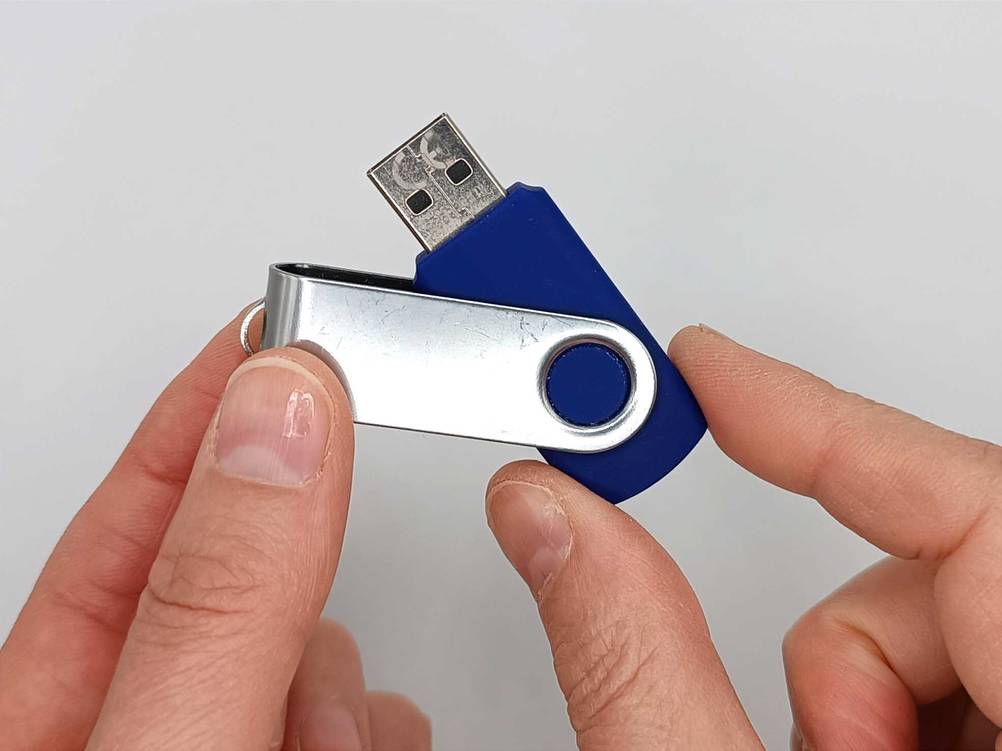 Zwei Hände halten einen getesteten USB-Stick zwischen den Fingern.