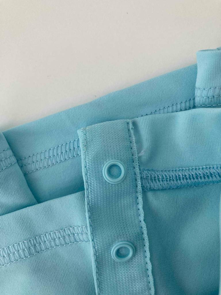 Detailansicht einer Kunststofföse im Ausschnittbereich eines hellblauen UV-Shirts für Kinder im Test.