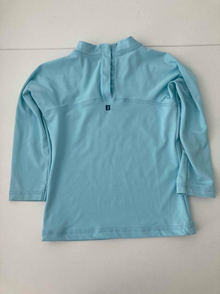 Das hellblaue getestete UV-Shirt für Kinder liegt ausgebreitet auf einer weißen Oberfläche.