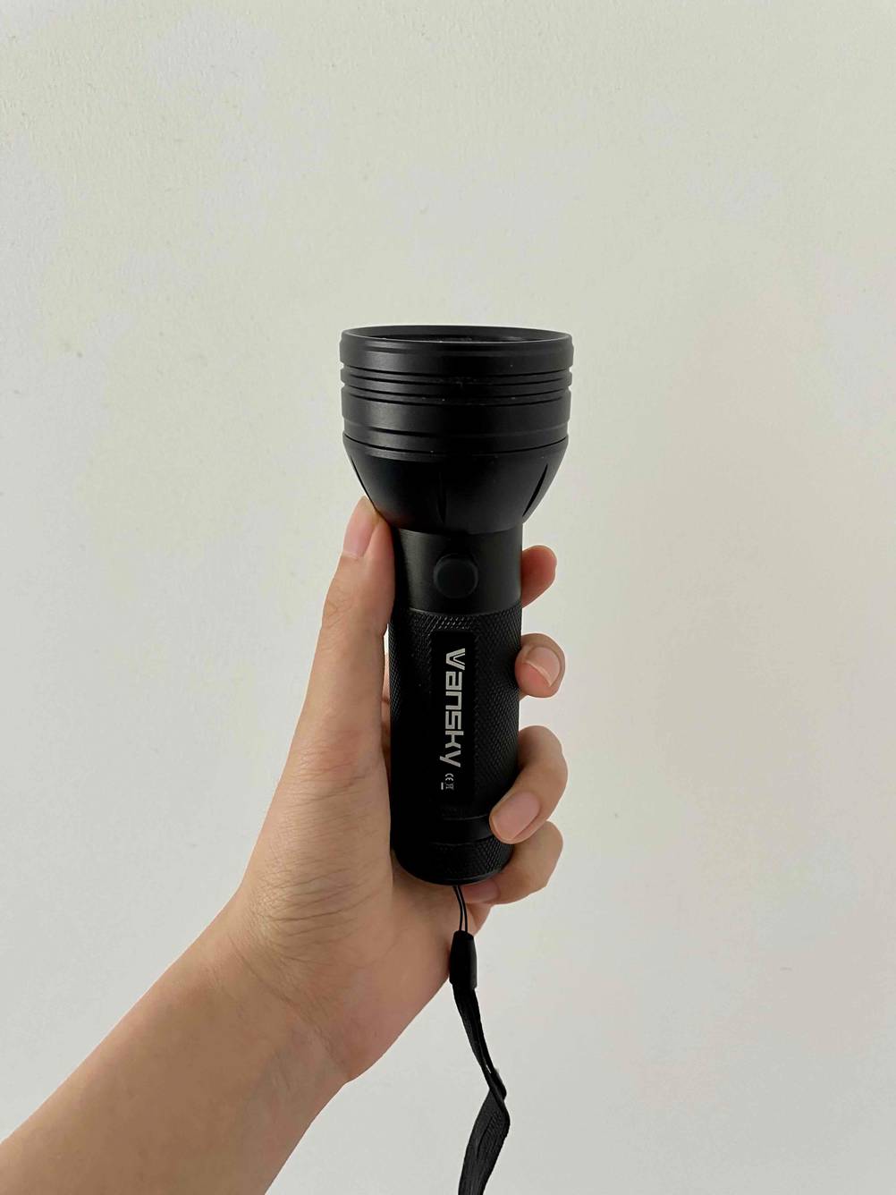 Eine Hand hält eine UV-Taschenlampe im Test seitlich vor eine hellen Wand.