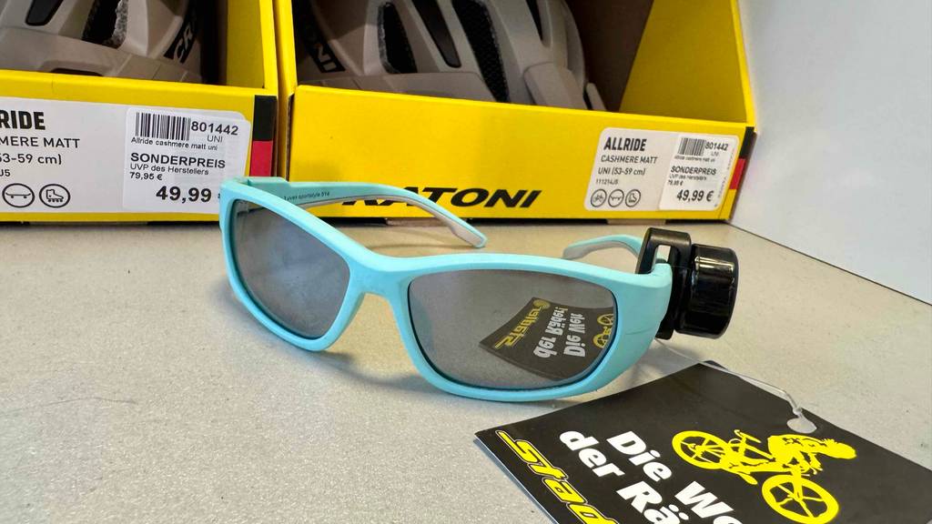Im test: Die Kinder-Fahrradbrille mit getönten Gläsern und türkisfarbenem Vollrand liegt vor einem gelben Produktkarton.