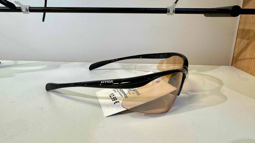 Seitenansicht auf die getestete Fahrradbrille mit schwarzem Halbrand, die ausgestellt auf einem weißen Regal liegt.