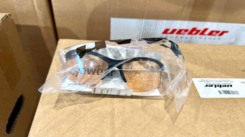 Die getestete Fahrradbrille mit schwarzem Halbrand liegt eingepackt auf einem braunen Karton.
