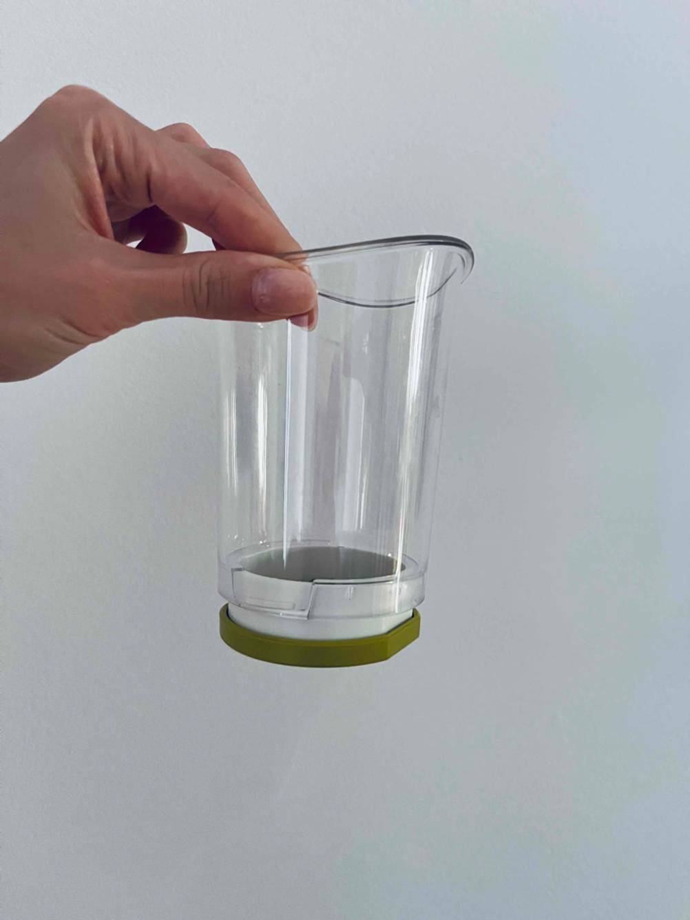 Hand hält mit zwei Fingern einen getesteten Zwiebelschneider vor einer weißen Wand.