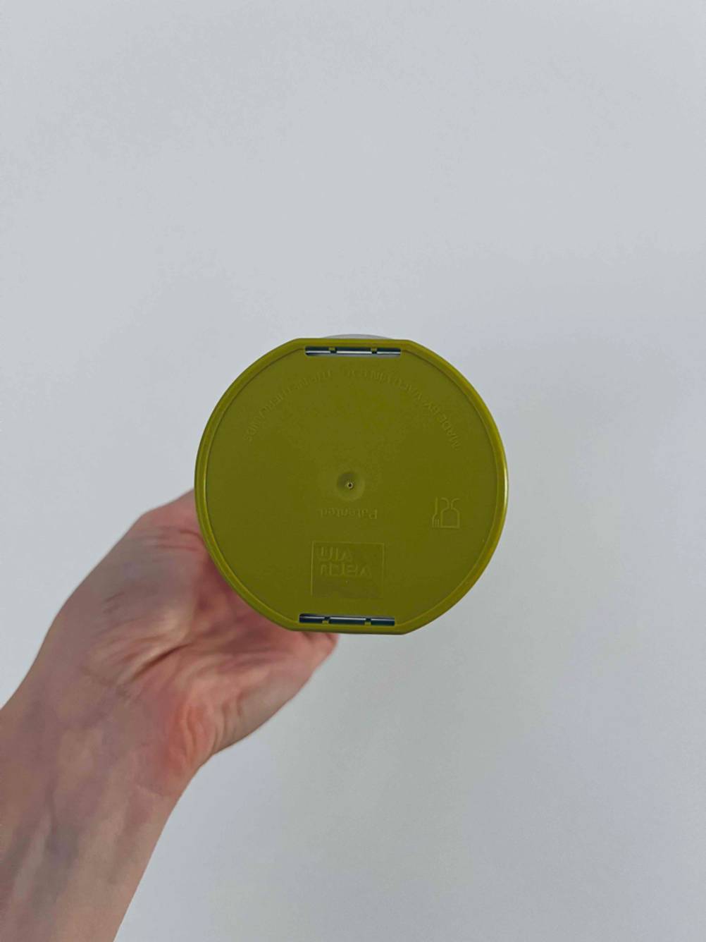 Hand zeigt die grüne Unterseite eines getesteten Zwiebelschneiders vor einer weißen Wand.