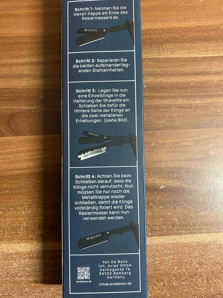 Eine Verpackung inklusive aufgedruckter Anwendungsbeschreibung eines Rasiermessers im Test liegt auf einer Holzoberfläche.