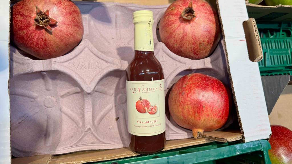 Getestet: Der Bio-Granatapfelsaft in der Flasche befindet sich auf einer Kartonage mit frischen Granatäpfeln.