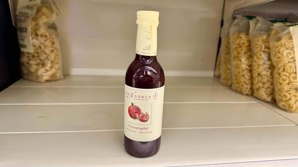 Eine Flasche mit getestetem Bio-Granatapfelsaft steht auf einem Regal neben Nudelpackungen.