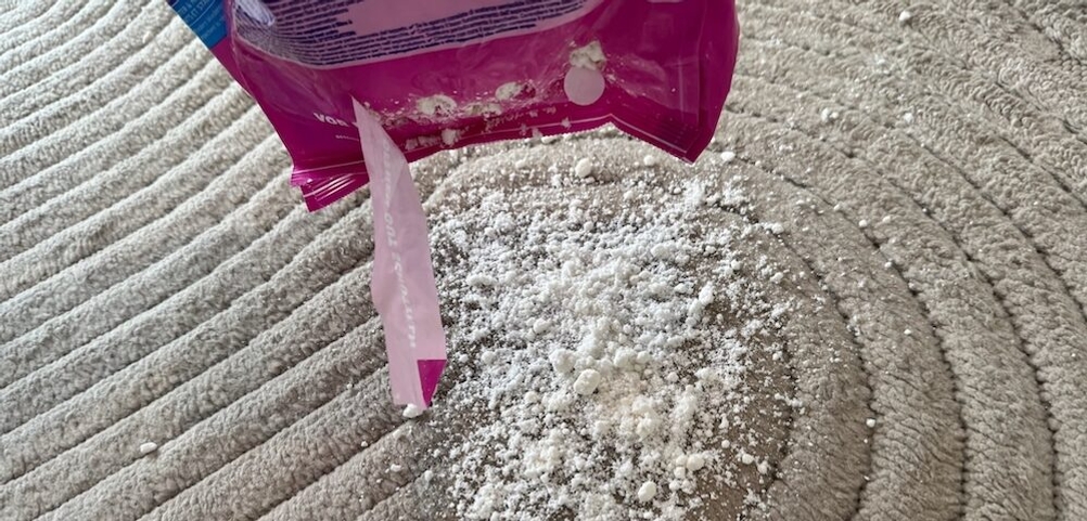 Vanish-Teppichreiniger-Pulver wird auf einen Teppich gestreut.
