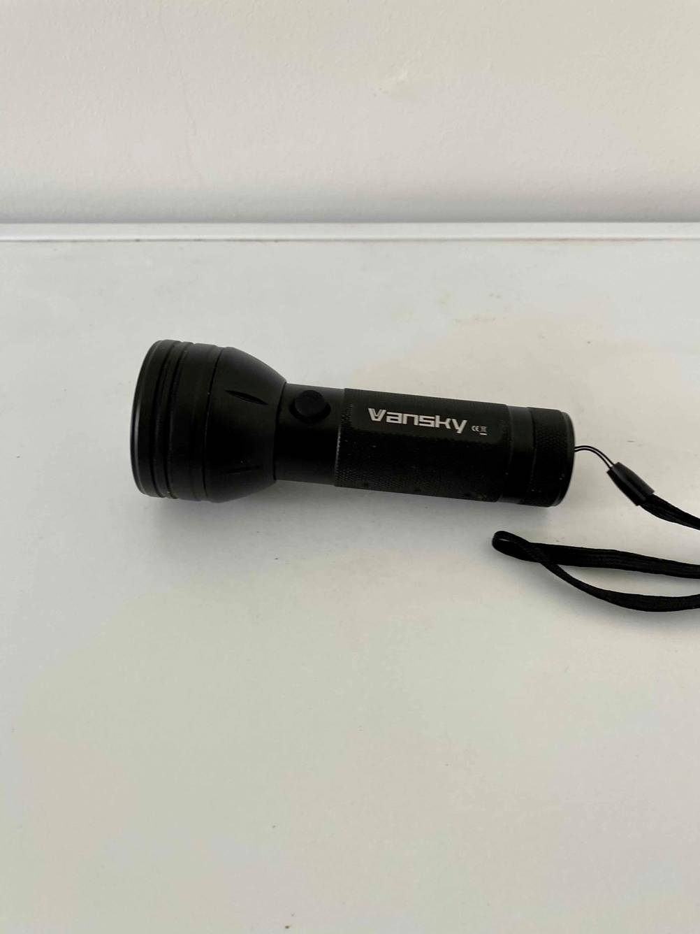 Eine getestete UV-Taschenlampe von schräg oben auf einer hellen Fläche liegend.