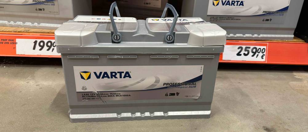 Getestet: Eine 150-Ah-AGM-Batterie fürs Wohnmobil steht, von vorn betrachtet, vor einem Regal mit mehreren Batterien.