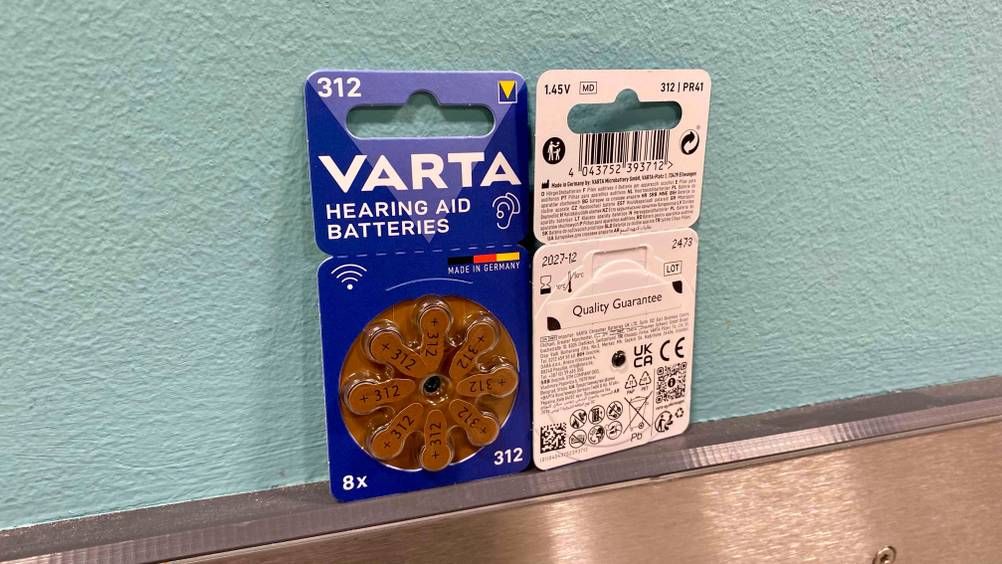 Zwei Packungen der getesteten Hörgerätebatterien-312 eine von vorne eine von hinten an einer hellblauen Wand lehnend.