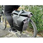 Die Vaude Aqua Back Tasche montiert am Gepäckträger, während eine Person auf dem Fahrrad sitzt. Die Tasche ist vollständig geschlossen.