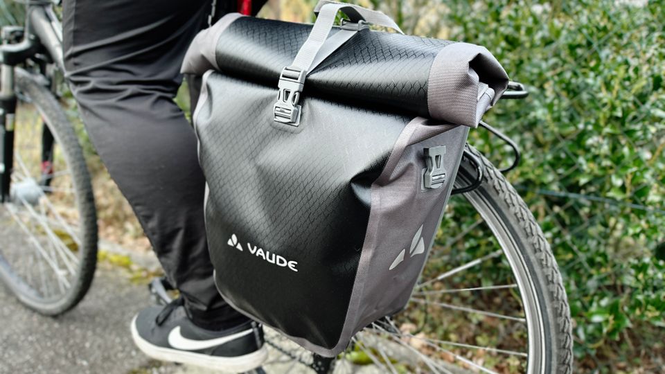 Die Vaude Aqua Back Tasche montiert am Gepäckträger, während eine Person auf dem Fahrrad sitzt. Die Tasche ist vollständig geschlossen.