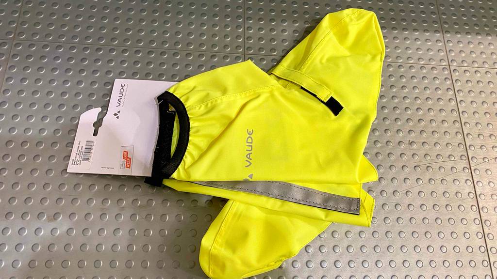Leuchtend gelbe Vaude Fahrrad-Überschuhe im Test liegen mit Fokus auf ihren rückwärtigen reflektierenden Streifen auf einem hellgrauen Noppenboden.