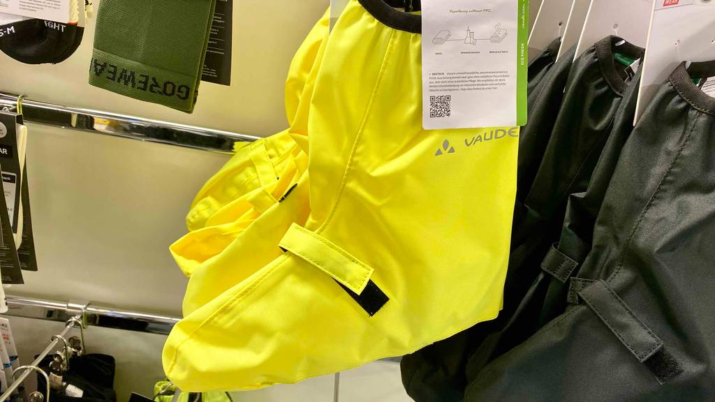 Gelb leuchtende Vaude Fahrrad-Überschuhe im Test hängen an einem Verkaufsstand neben einem dunkelgrünen Modell.