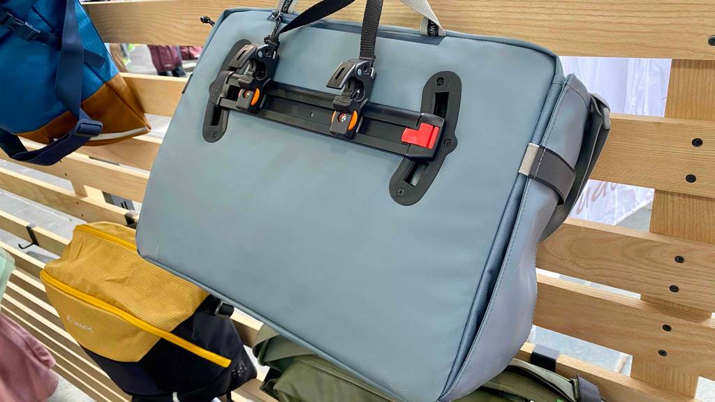 Büro-Fahrradtaschen im Test: eine graue Fahrradtasche der Marke Vaude von hinten betrachtet mit Befestigungsschiene für den Gepäckträger oder das Lenkrad an einem Holz-Ausstellungsregal.