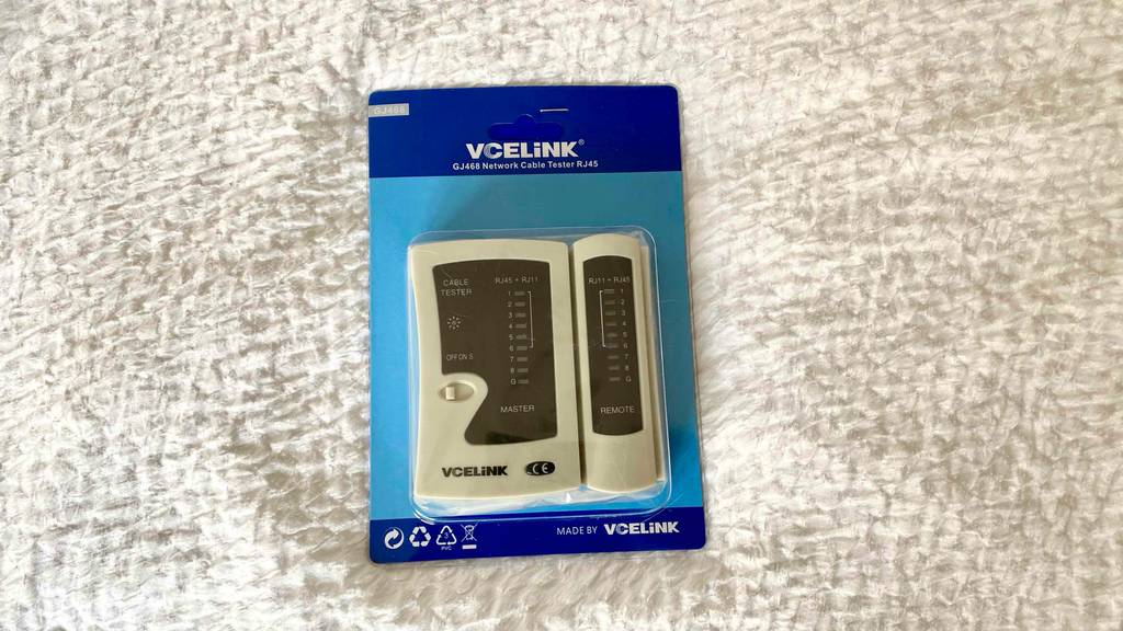 Ein getesteter Kabeltester RJ45 der Marke VCLiNK liegt in seiner Verpackung auf einer weißen Oberfläche.