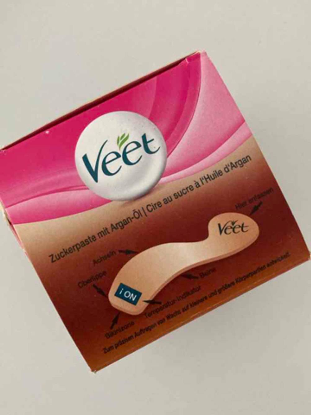 Zuckerpasten im Test: Eine VEET-Packung inklusive der Zuckerpaste mit Argan-Öl liegt auf einer beigefarbenen Oberfläche.