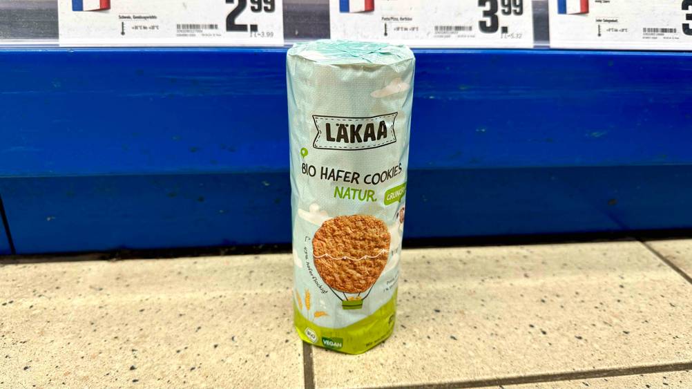 Eine Packung der veganen Kekse vor einem Verkaufsregal mit Preisschildern auf dem Boden stehend.