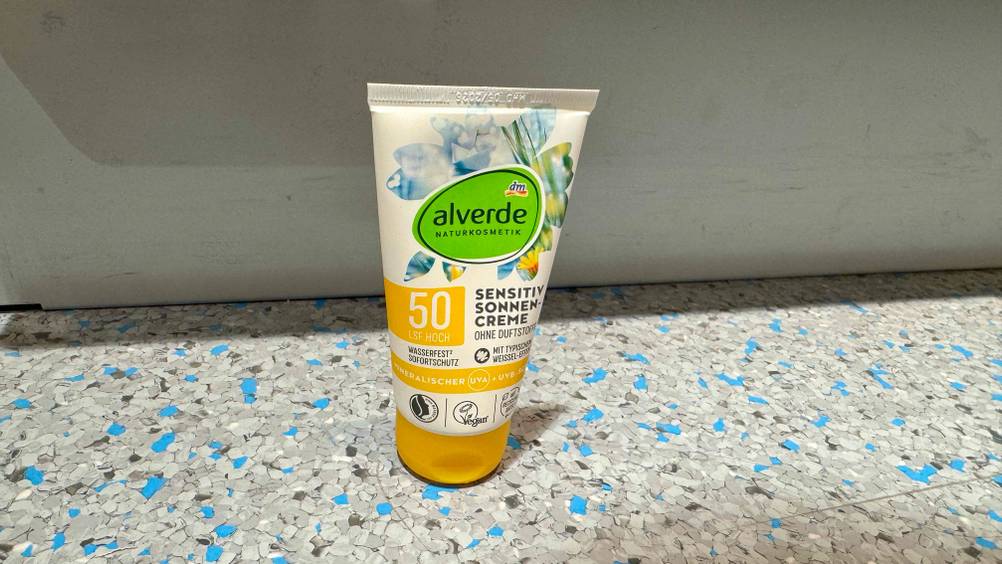 Eine Tube der veganen Sonnencreme im Test auf einem grau-blauen Boden stehend.