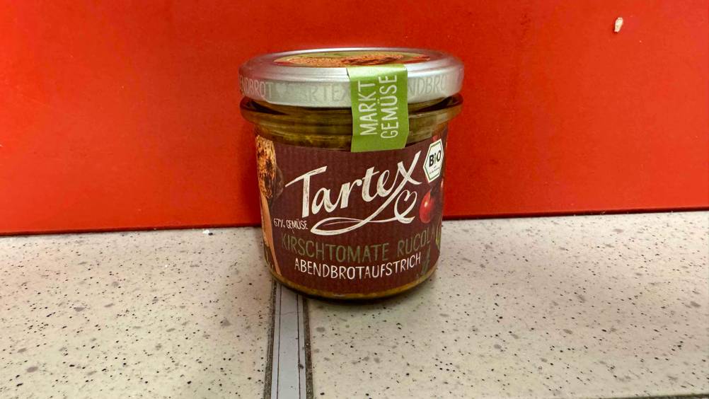 Veganer Brotaufstrich im Test: Ein Glas vor einer roten Wand auf dem Boden.