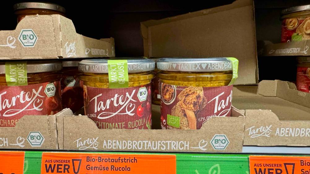 Mehrere Gläser des getesteten veganen Brotaufstrichs stehen in Kartons in einem Verkaufsregal.