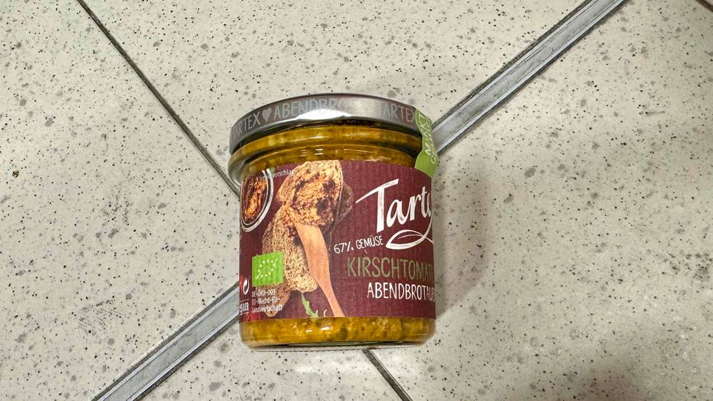 Veganer Brotaufstrich getestet: Ein Glas liegt auf einem Fließenboden.