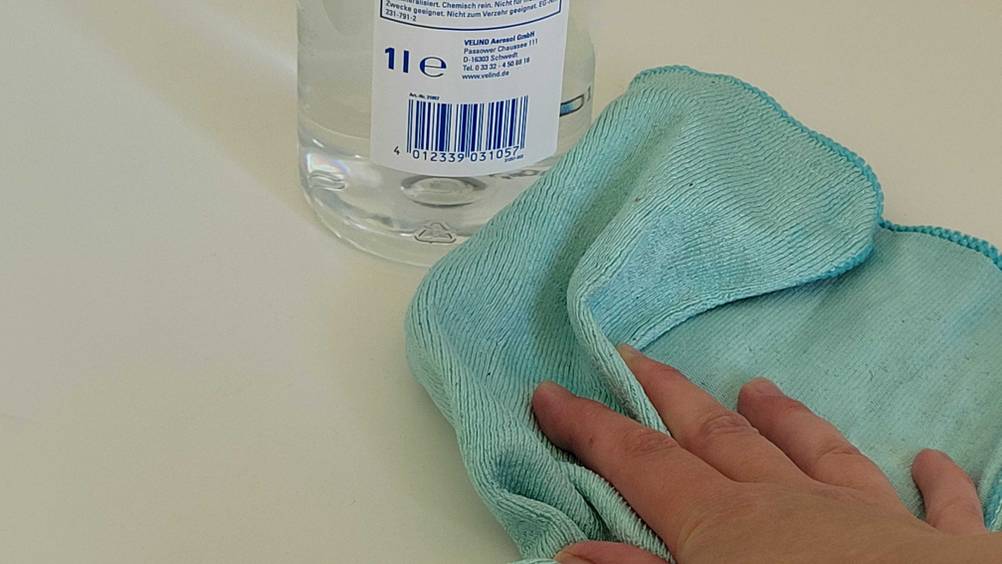 Eine Hand wischt mit einem Tuch vor einer Flasche getestetes destilliertes Wasser.