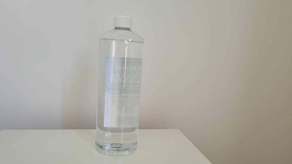 Rückseite einer Flasche getesteten Destilliertes-Wassers vor einer hellen Wand.