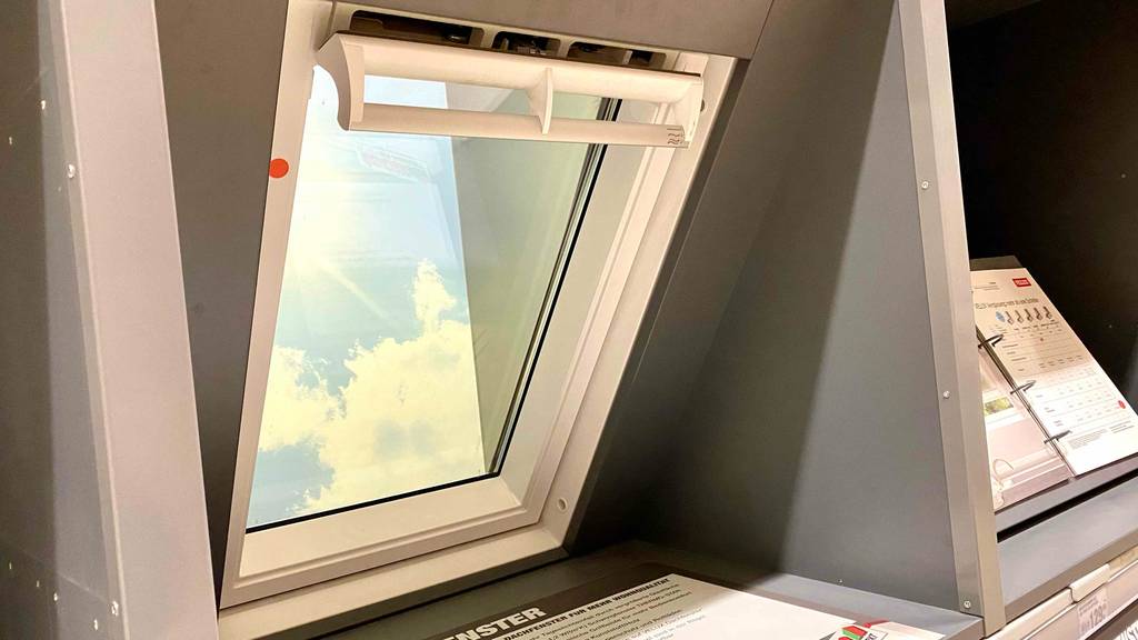 Dachfenster-Test: weißes Dachfenster im geschlossenen Zustand in einem Verkaufsbereich neben ausgestellten Produktinformationen.