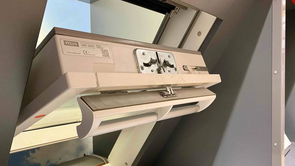 Detailaufnahme vom Schließmechanismus eines weißen geöffneten Velux Schwing-Dachfensters im Test, das in einem Geschäft ausgestellt ist.