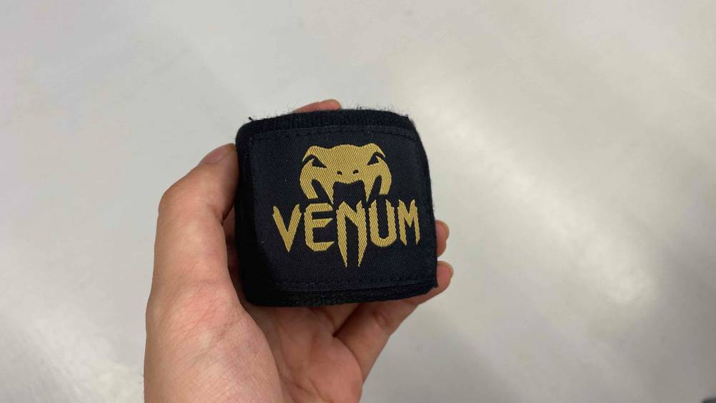 Im Test: Eine Hand hält eine Boxbandagen mit Logo vor eine helle Fläche.