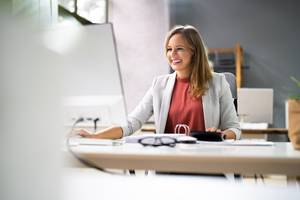 Vereinssoftware-Test: Eine Frau schaut lächelnd auf ihren PC, während Sie am Schreibtisch sitzt.