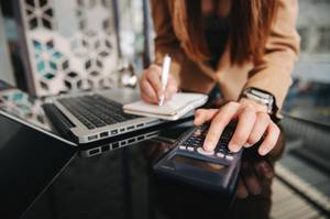 Vereinssoftware-Test: Eine junge Frau rechnet auf einem Taschenrechner und macht dabei Notizen.