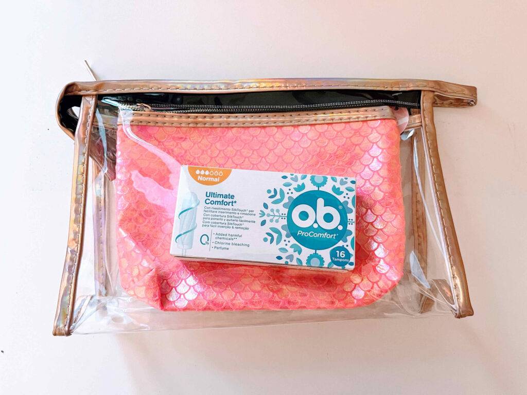 Eine weiße Schachtel mit getesteten Tampons ProComfort der Marke o.b. in einem transparenten Kulturbeutel, der sich vor einem weißen Hintergrund befindet.