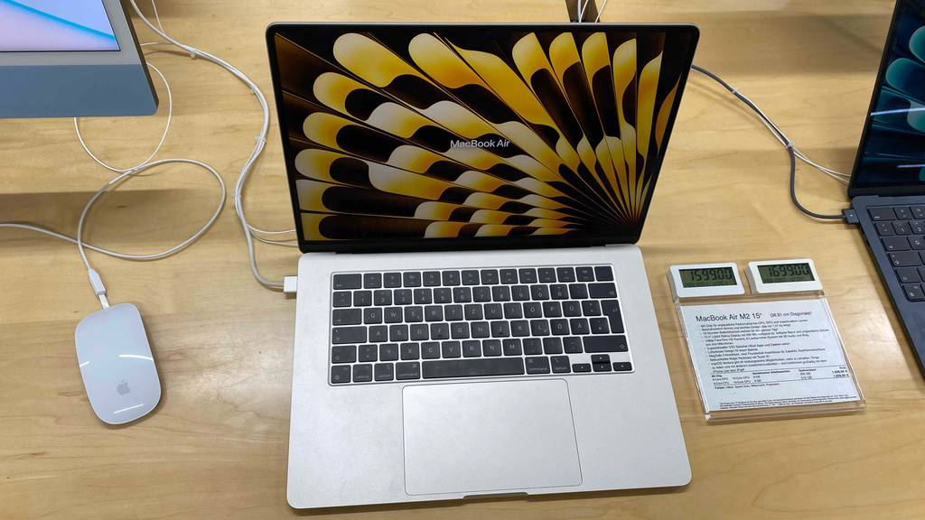 Gesamtansicht eines getesteten 15-Zoll-Laptops: ein geöffnetes MacBook Air von Apple in Weiß steht auf einem Verkaufstisch neben einem Preisschild und einer Maus.