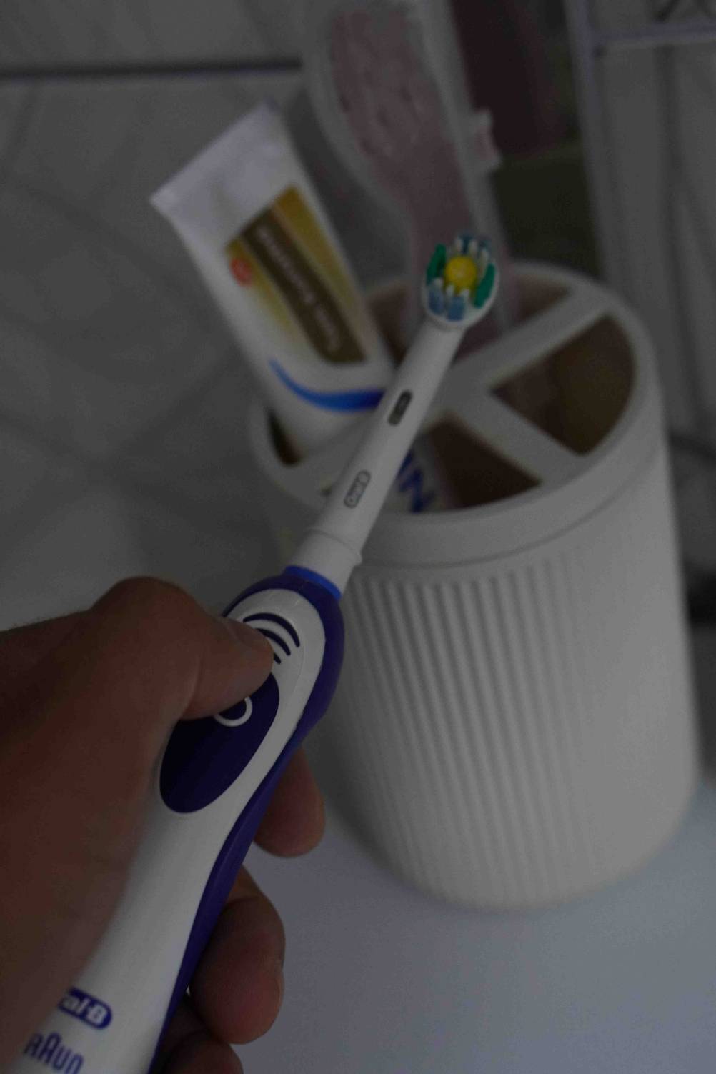 Hand hält getestete elektrische Zahnbürste von Oral-B vor einem Zahnbürstenbecher mit Zahnpasta.